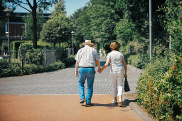 Fototapeta na wymiar old couple walking hand in hand on street in front of trees