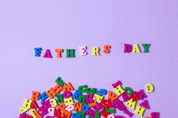 Child's toy letters spelling Fathers Day next to randomly lying letters on purple background.