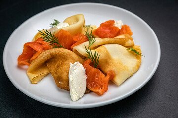 Pancakes with goat cheese and salmon on a dark table
