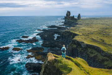 Man hiker in yellow jacket stand on the peak of the rock in outdoor park in Iceland. Londrangar