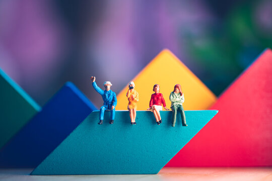 Miniature people, man and woman sitting on colorful wooden block using as business and social concept