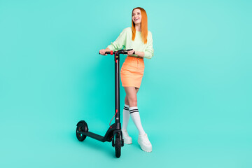 Full length photo of charming happy dreamy woman look empty space hold scooter isolated on teal color background