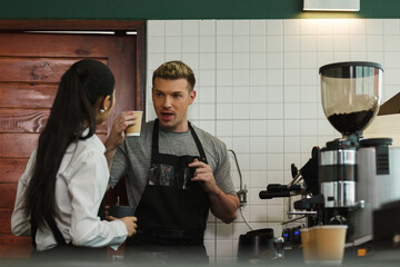 Barista man and women wearing apron holding coffee cup and thumbs up looking at camera in counter at coffee shop. startup success make store coffee.