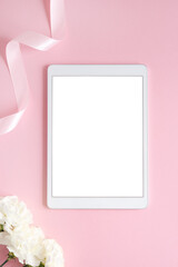 Minimal feminine flat lay with pink and white flower and tablet with empty screen. Styled mock up top view on pale peach background. Device