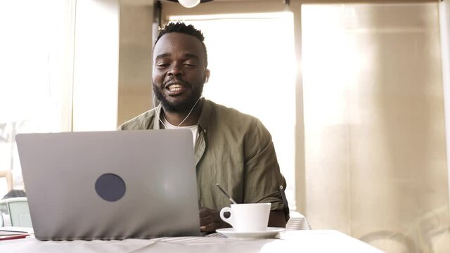 Young african man doing a video call using computer laptop at pub bar restaurant