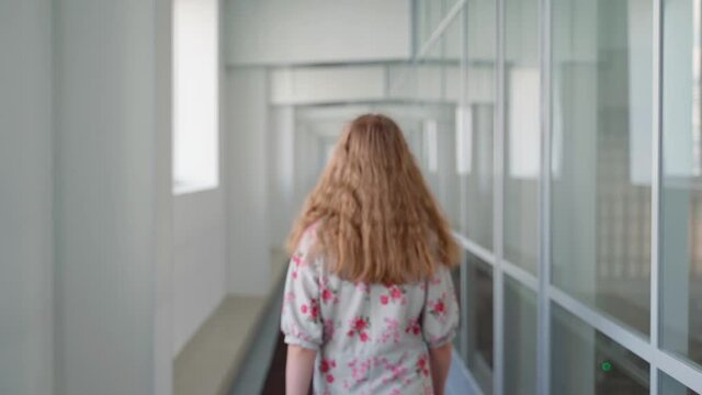Unrecognizable girl walk along corridor until out of focus indoors. Young adult woman in office place walking