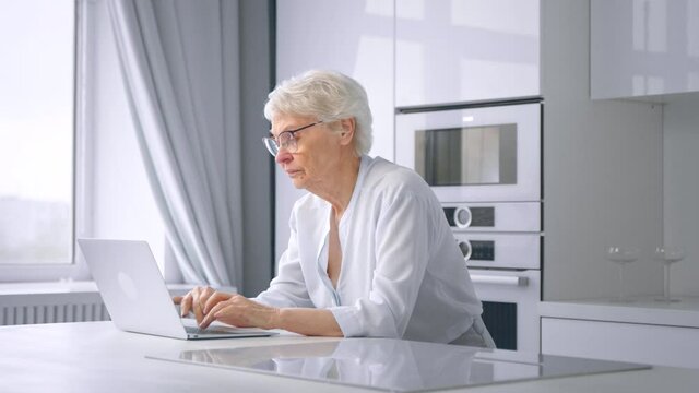 Depressed pensioner businesswoman types on grey laptop