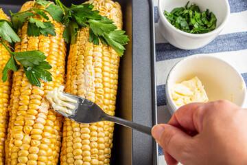 Step by step recipe. Home cooking baked corn in foil. Step2 female hand smears butter to corn. Homemade food concept. Vegetarian healthy eating.