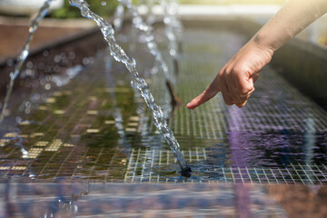 Kid plays in city fountain. Stream, splash of clean water on hand.  Refreshing water in summer heat...
