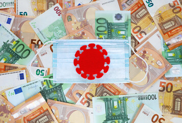 Red felt covid virus centered on blue medical mask on 50 and 100 euro banknotes background....