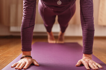 The girl does yoga in the asana stand on a lilac mat.