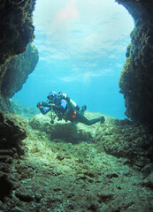 A scuba diver enters the entrance of a cave. The diver begins his dive underwater