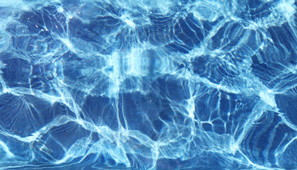 Azure rippled water surface of swimming pool. Background of water ripple under bright sunny sky. Grainy bottom texture under water. Summer vacations resort concept. Banner with place for text.