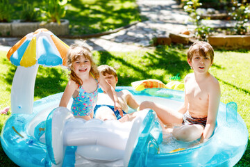 Three kids, two boys and toddler girl splash in an outdoors swimming pool in summer. Happy...