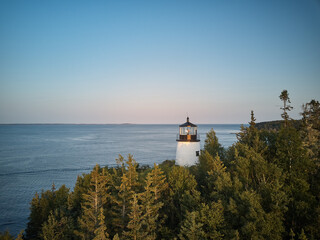 Fototapeta na wymiar Aerial drone image of the Owls head Lighthouse surrounded by pristine forest on the cliffs overlooking the entrance to Owls Head Harbor on the Maine Coast at sunset
