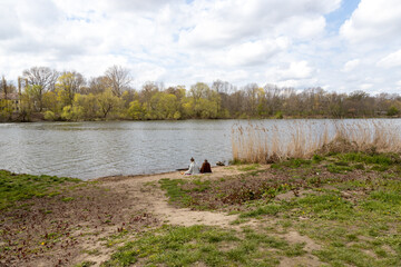 Two women sit on a blanket on the beach of a river and talk