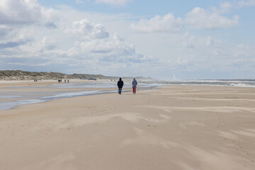 People walking on the beach with remnant of water between the sea and the dunes, day with a blue sky with abundant white clouds in Hargen aan Zee, North Holland, Netherlands. In time of coronavirus