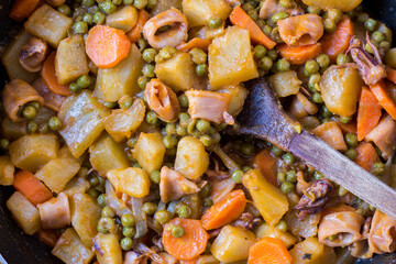 Squid with potatoes, peas and carrots cooked in a pan on wooden background