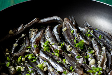 Fresh anchovies to be cooked in a pan with garlic and parsley. Wood background.