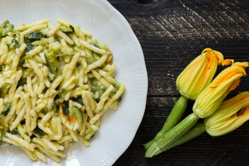 Trofie, Italian pasta with courgette flowers and zucchini on dark wooden background