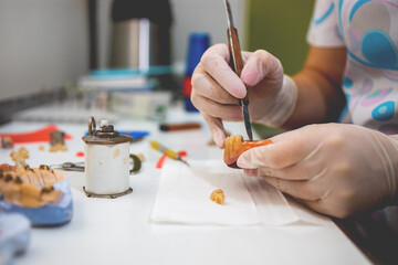 Close-up of a dental technician shaping a prosthesis tooth with a tool at work desk.