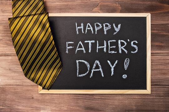 Happy fathers day on chalk board and colorful tie laid on dark wooden backround.