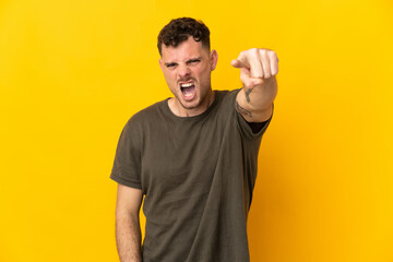 Young caucasian handsome man isolated on yellow background frustrated and pointing to the front