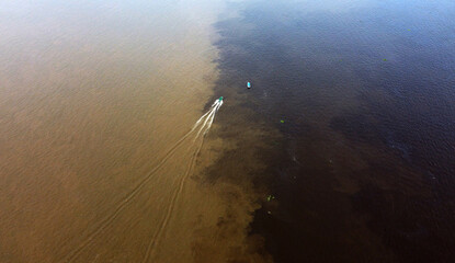 Boat navigates through the meeting of waters of Solimoes, left, and Negro rivers, near the city of...