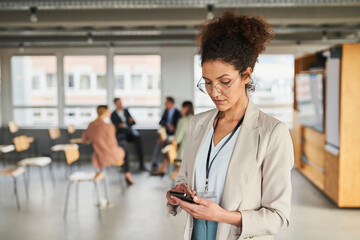 Female entrepreneur using mobile phone with colleagues in background at office