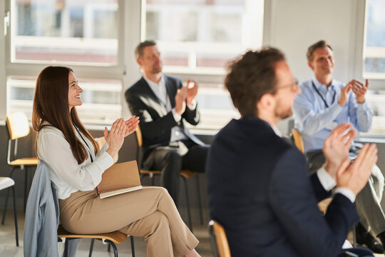 Businesswoman clapping hands with colleagues in education conference centre