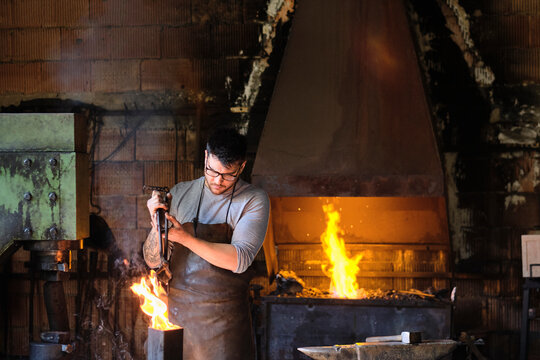 Young male blacksmith burning metal in fire at workshop