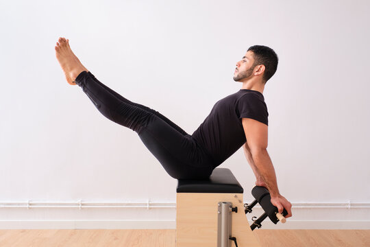 Concentrated man practicing pilates on chair by wall in exercise room