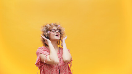 Beautiful girl listening to music on her headphones. Girl in a good mood wearing round spectacles and enjoying her favorite music. Isolated on bright yellow background. Music Lover. Enjoyment. 