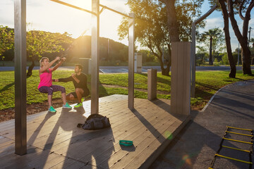 Personal fitness trainer and young woman client, corrects exercises with straps. In park in the morning. Sunny day.