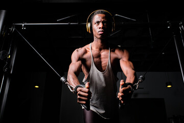 Determined young man listening music through headphones while practicing suspension exercise at gym