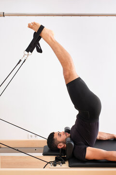Male athlete with legs raised practicing pilates on cadillac reformer in exercise room