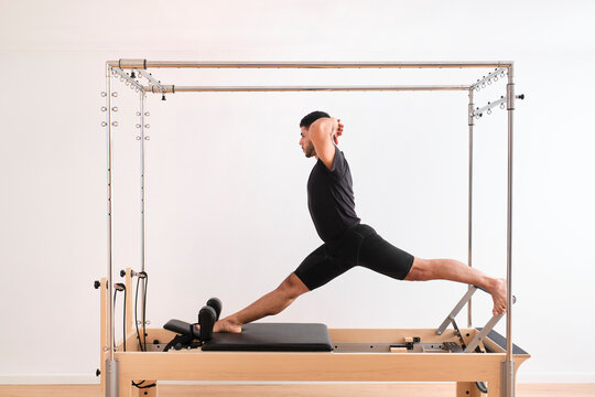 Male athlete with hands behind head practicing pilates on cadillac reformer in exercise room