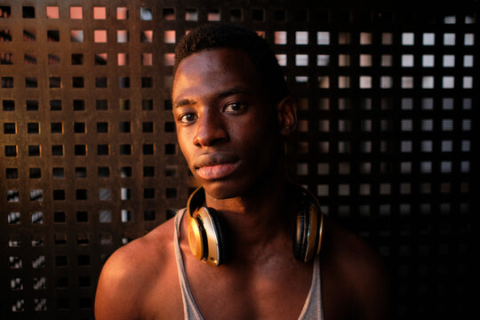 Young man with headphones around neck in front of metal wall at gym