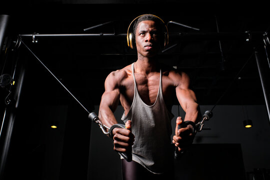 Determined young man listening music through headphones while practicing suspension exercise at gym