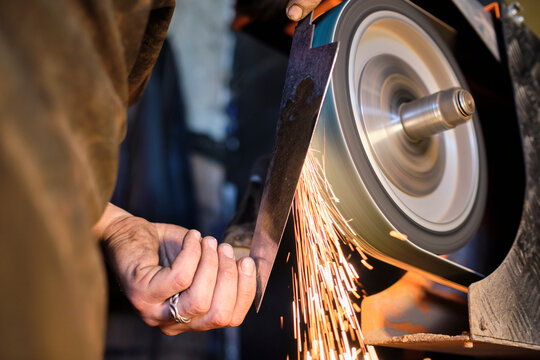 Male blacksmith sharpening knife shape metal on grinder at workshop