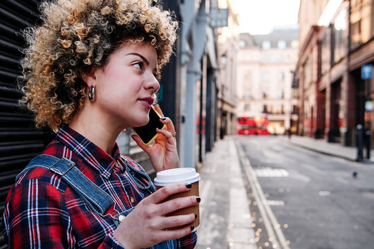 Curly haired woman having coffee while talking on smart phone