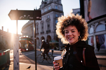 Smiling hipster woman having coffee during sunny day in city
