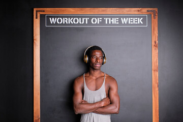 Thoughtful young man with headphones standing in front of black board at gym