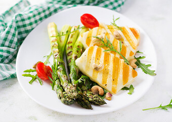 Grilled halloumi cheese salad with tomatoes and asparagus on plate on light background. Healthy vegetarian food.
