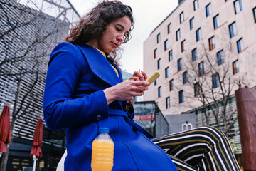 Businesswoman using smart phone while sitting by juice bottle