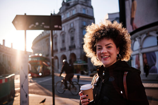 Smiling hipster woman having coffee during sunny day in city