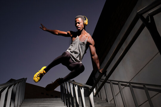 Young African man with headphones jumping at staircase