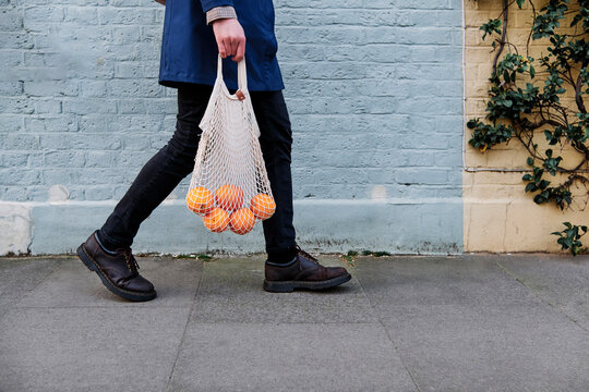 Man with bag of oranges walking on footpath by wall