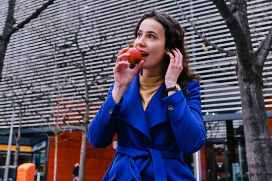 Businesswoman in trench coat eating apple