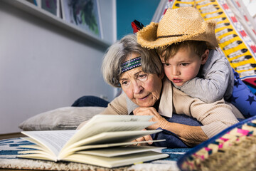 Senior woman reading book while boy lying on her at home